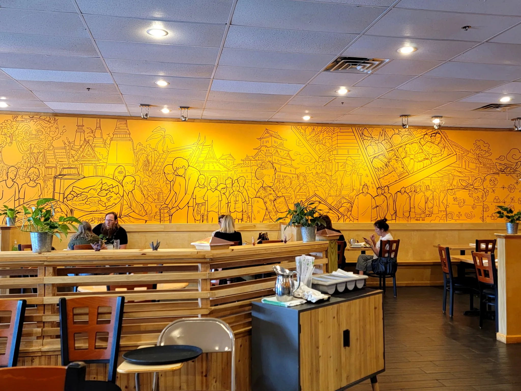 The hand-drawn mural wall inside Pin Toh Asian — Thai temples and street vendors in ink on amber