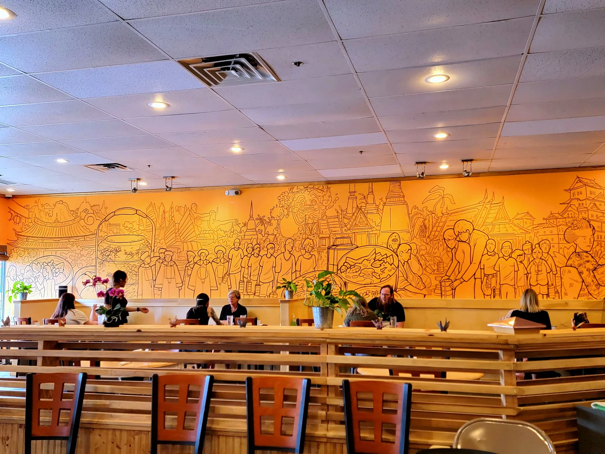 The dining room at Pin Toh Asian, guests seated along the mural wall
